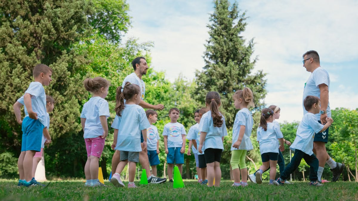 Group of children and teachers playing and learning in a sunny park setting.